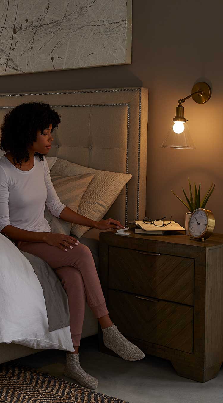 Woman sitting on bed, reaching for Pico pedestal remote on nightstand