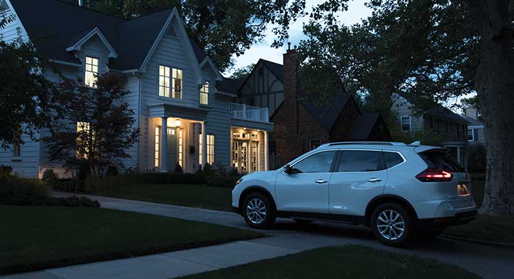 White car pulling into driveway of house with welcoming lights turned on.