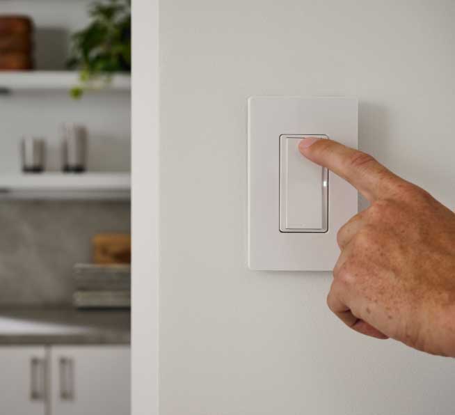 Man turning lights on with a Pico paddle remote mounted to the wall