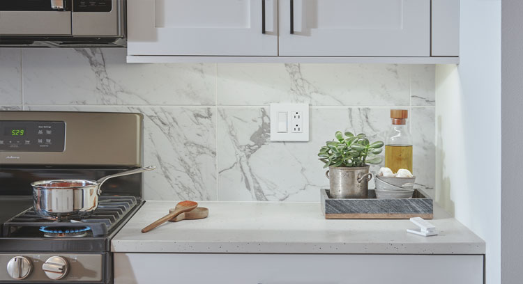 Woman reaching for Diva Smart Dimmer switch on kitchen wall.