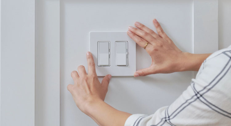 Woman reaching for Diva Smart Dimmer switch on kitchen wall.