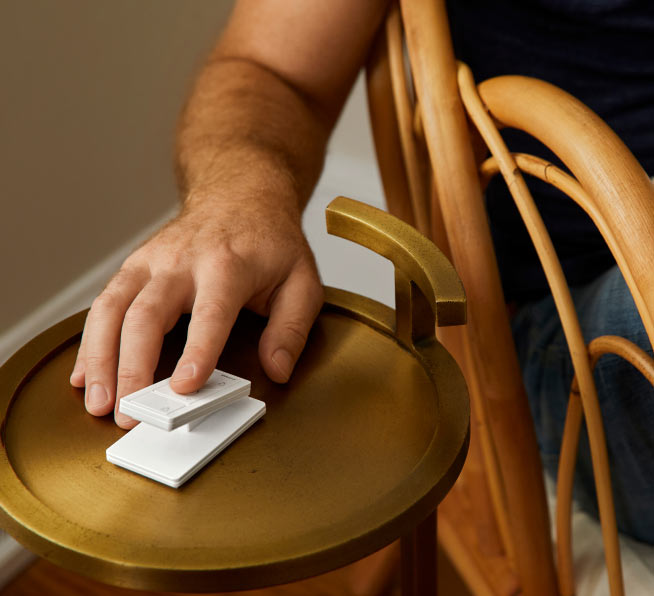 Man using 3-button with raise/lower Pico smart remote on side table