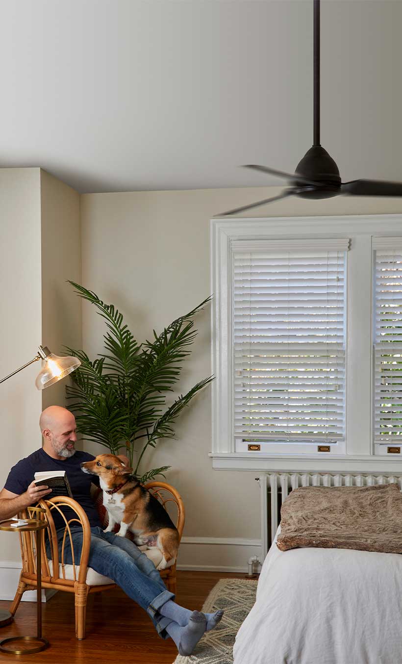 Man reclining on chair with dog and book in his arms besides Pico remote on side table.