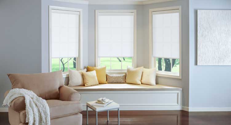 Modern home Living Room with couch, pillows, and three Serena Smart Roller Shades, lightly-colored