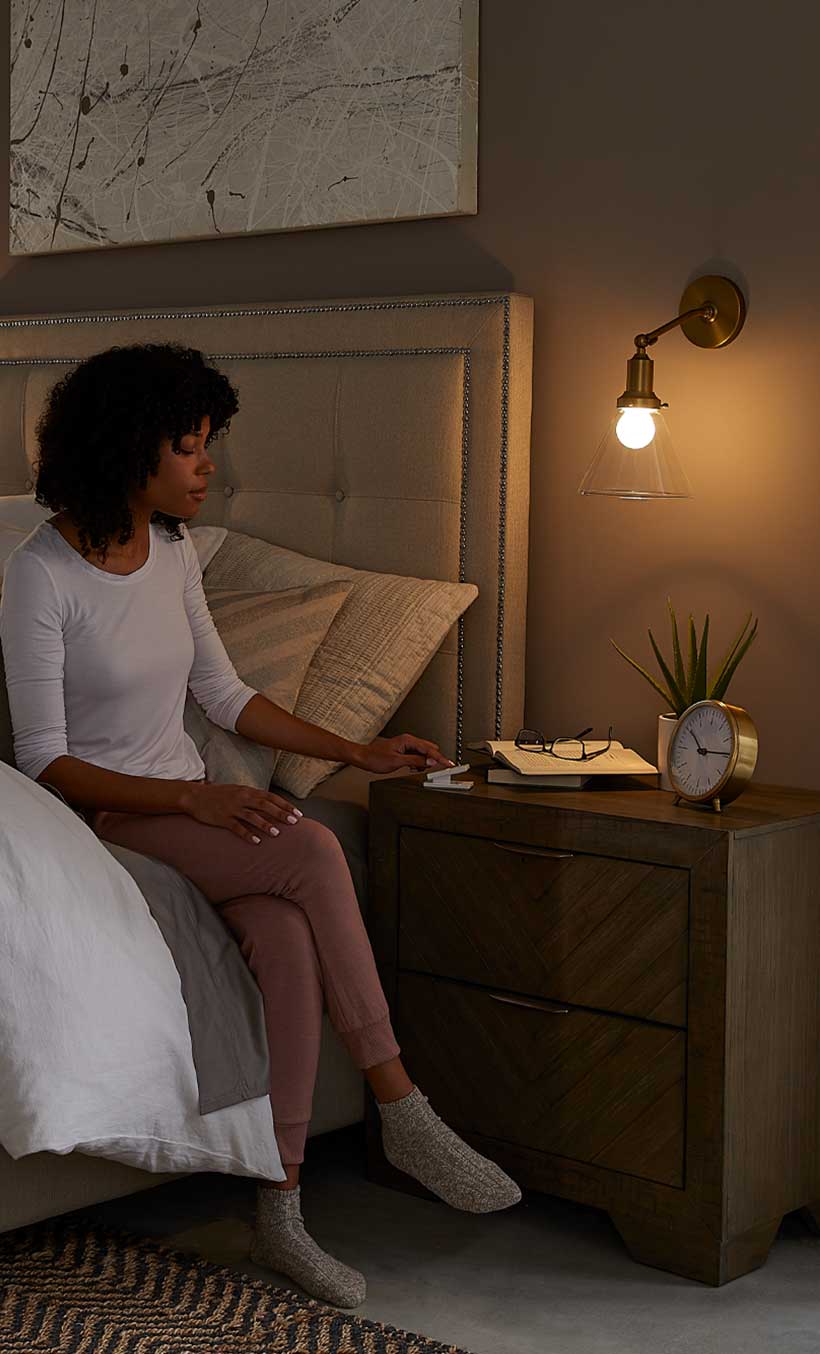 Woman sitting up in bed, reaching for Pico Remote Pedestal on her bedside table