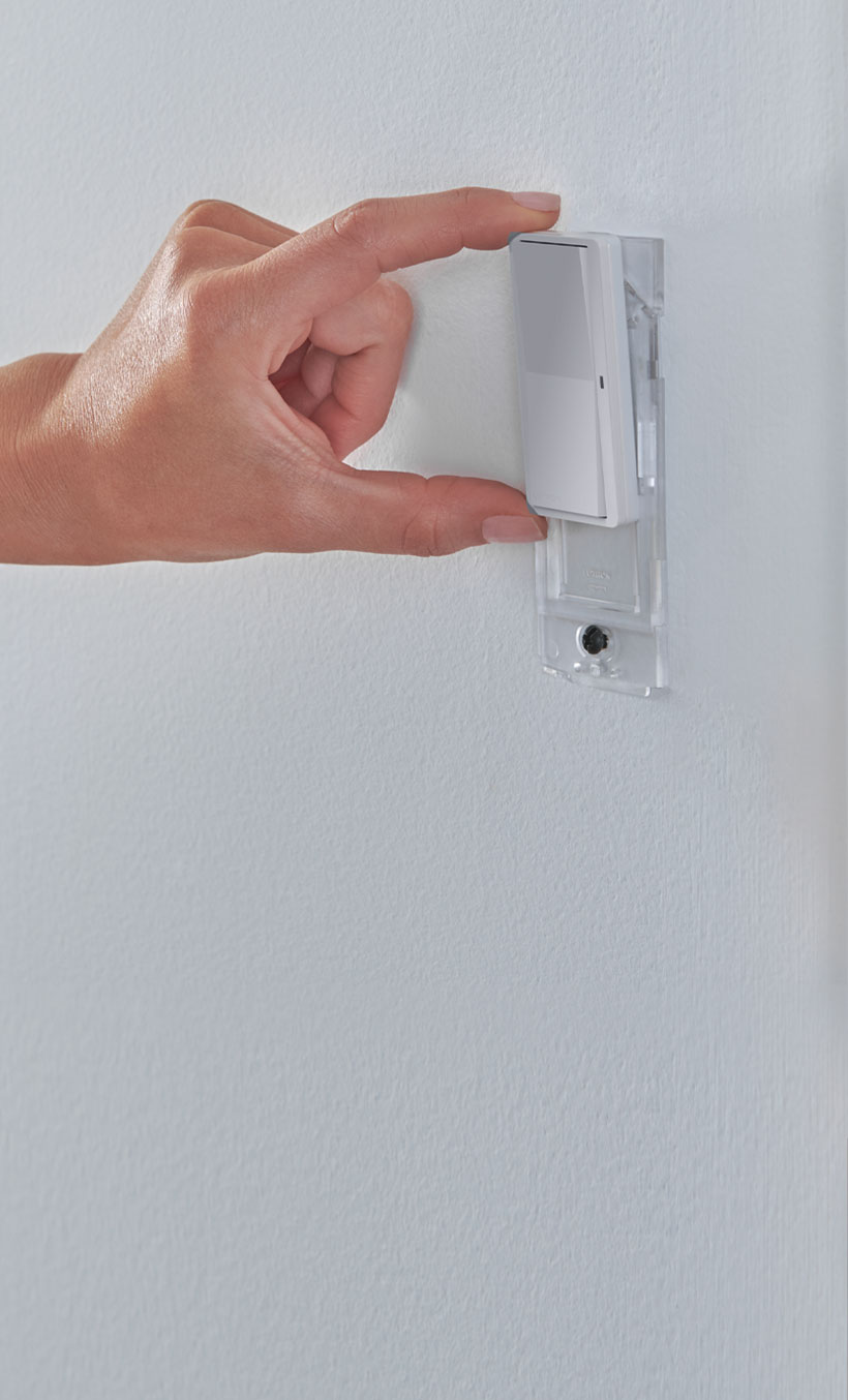 Male hand holding Pico Paddle Remote, pointing towards dimmer switch on wall