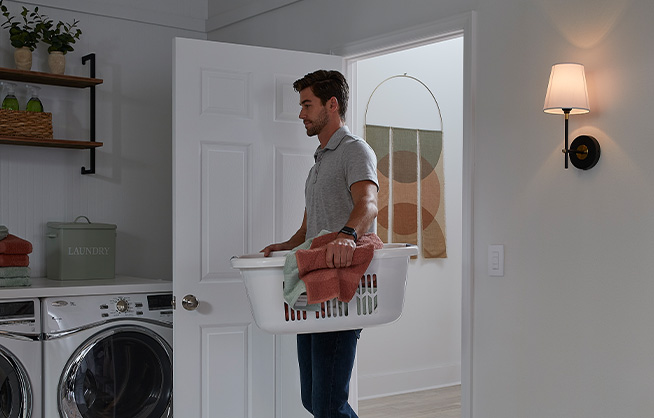 Man carrying laundry basket walking into large, well-lit laundry room