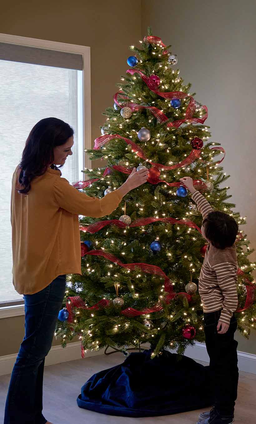 Mother and son decorate Christmas tree with lights by fireplace