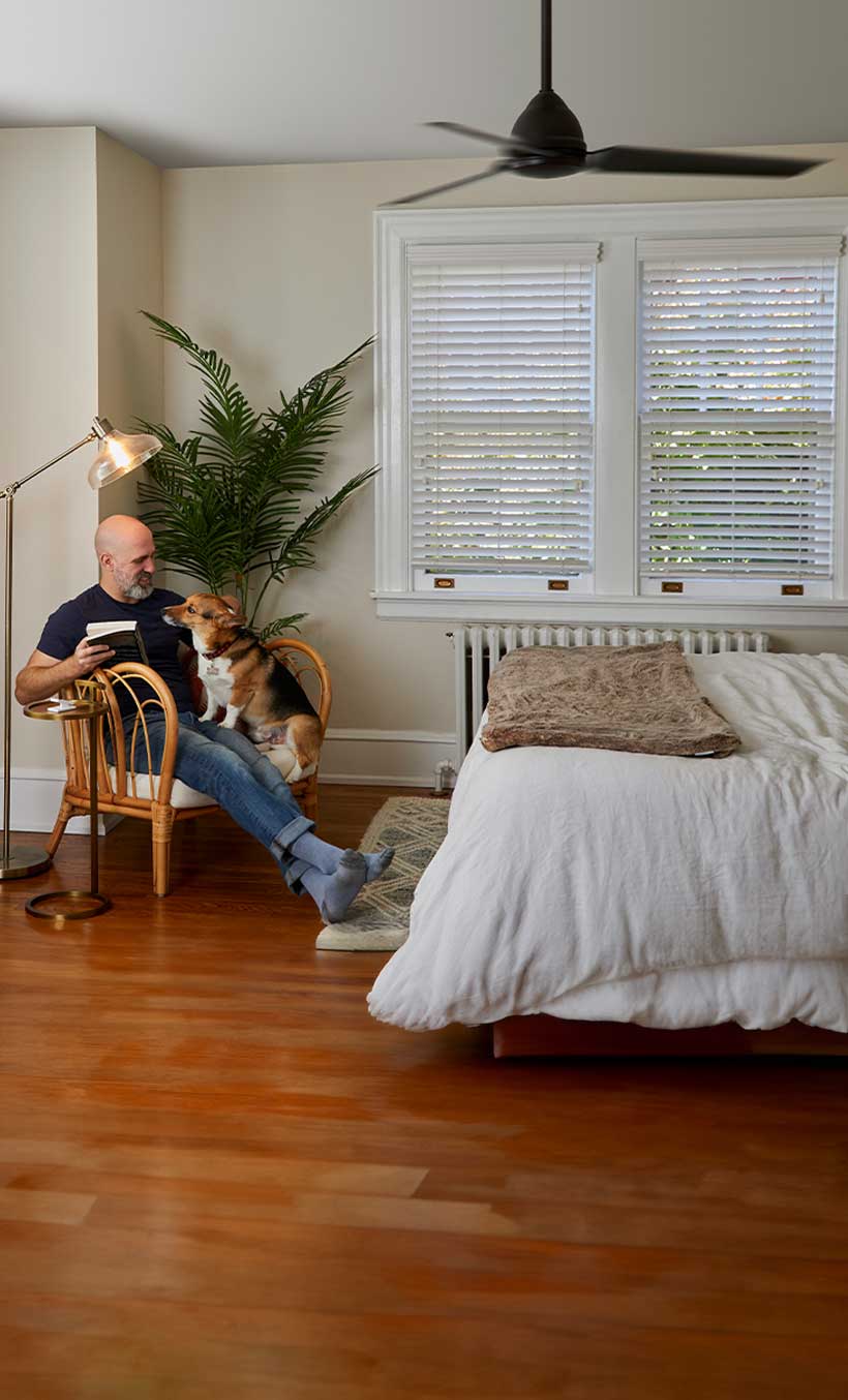 Man sitting on chair with a book and his dog on his lap, with Pico Remote Pedestal on side table