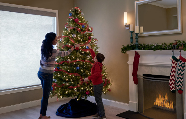 Mother and son decorate Christmas tree with lights by fireplace