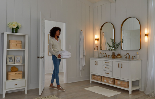 Woman carrying towels walking into large, well-lit bathroom