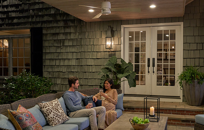 Man and woman sitting on outdoor patio beneath overhead ceiling fan.