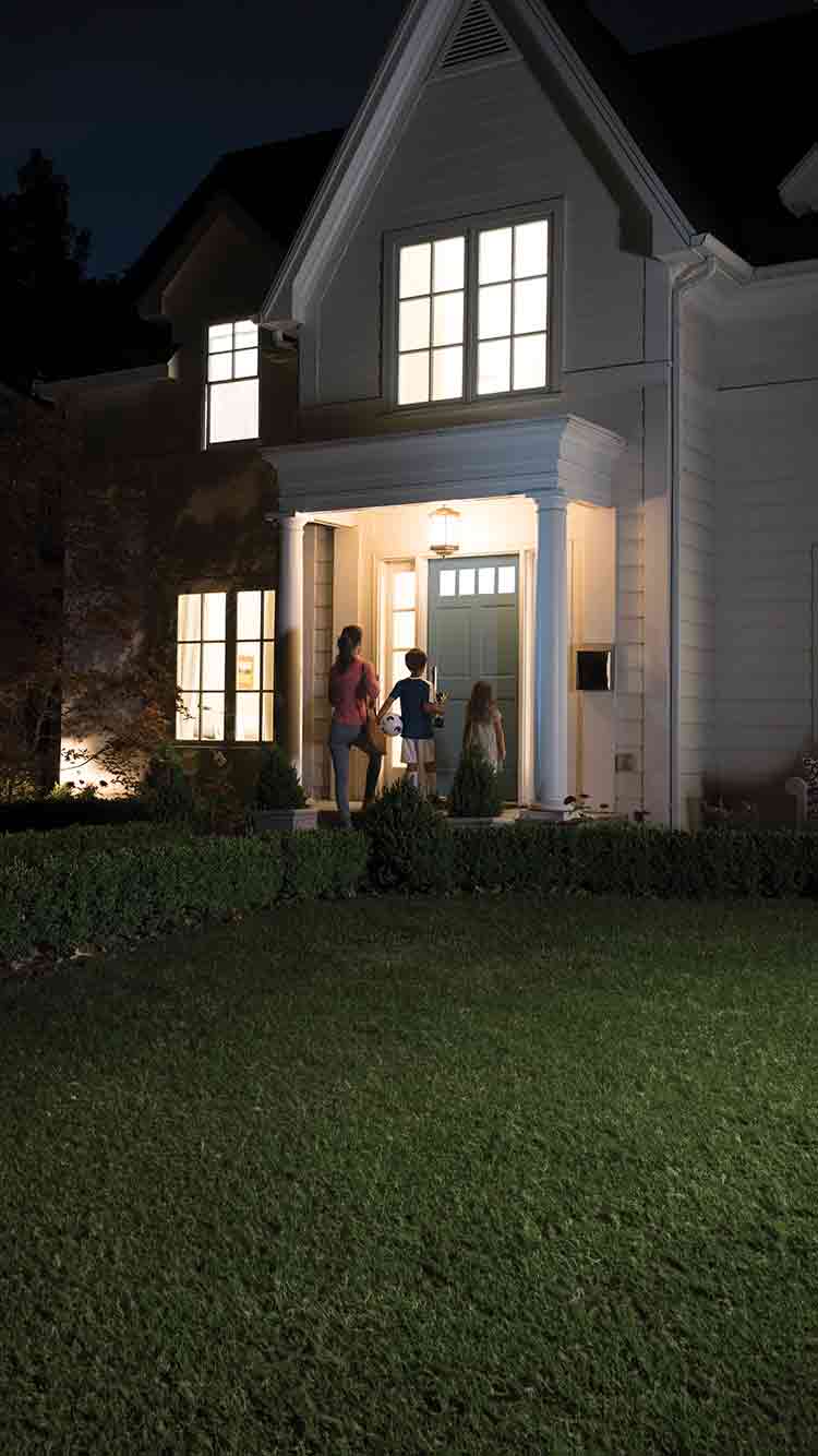 Mom and children arriving home with smart indoor lighting visible through windows