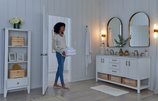 Woman carrying towels walking into large, well-lit bathroom