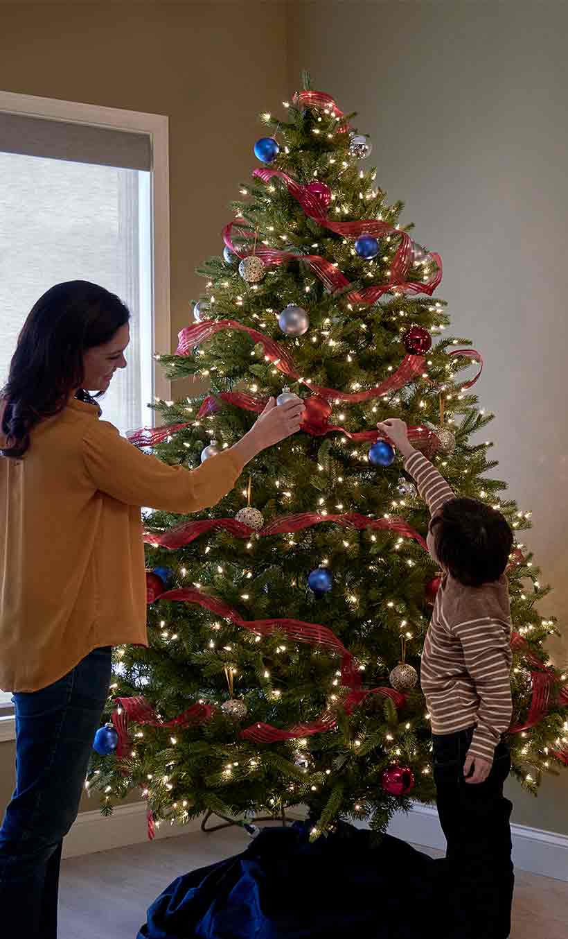 Mother and son decorate Christmas tree with lights by fireplace