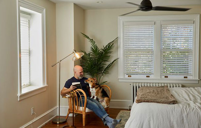 Man sitting on chair with a book and his dog on his lap, with Pico Remote Pedestal on side table