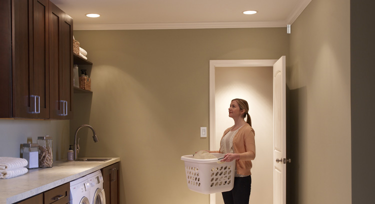 Woman walking into a well-lit laundry room with a basket of laundry