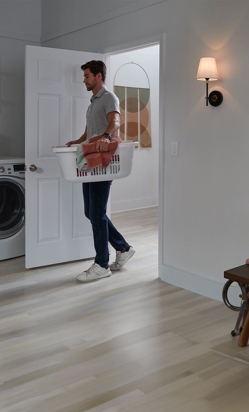 Man carrying laundry basket walking into large, well-lit laundry room